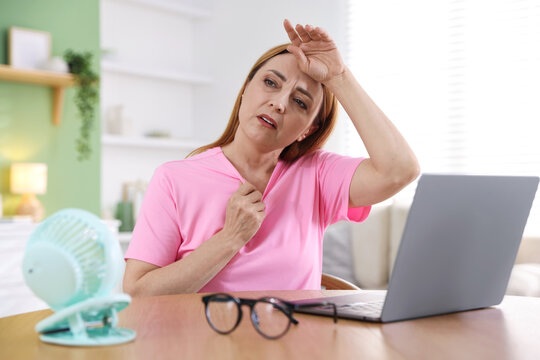 Menopause. Woman suffering from heat flash while working on laptop at table indoors