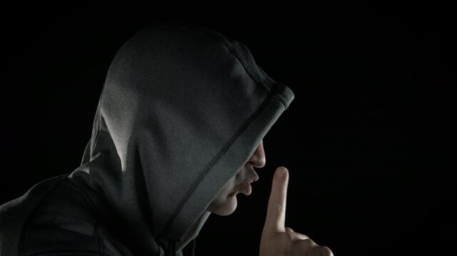 Man in hood with stop gesture in black. Man suspected show the stop gesture with his finger against black background