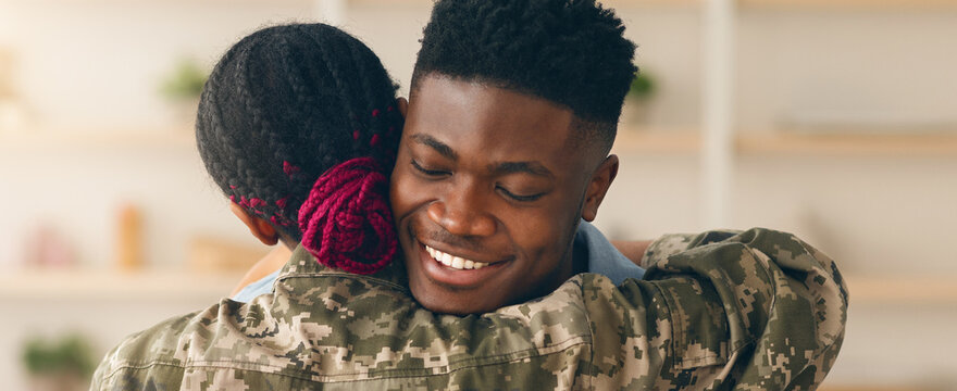 A soldier embraces a loved one during a homecoming event inside a bright room. They share a joyful moment filled with warmth and connection, celebrating their reunion after a long time apart.