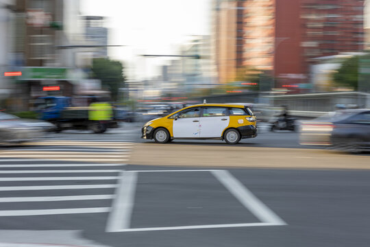 View of a yellow and white taxi cab driving through a busy urban intersection with motion blur and city buildings in the background Taipei City, Taiwan.