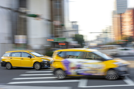View of yellow taxis driving through a city intersection with motion blur and urban buildings in Taipei City, Taiwan.