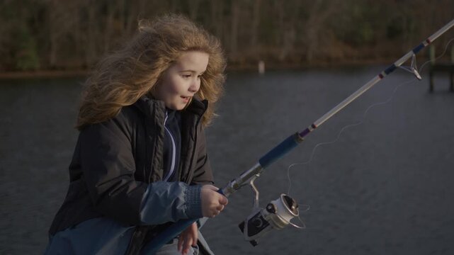 Child enjoys fishing by quiet lake. Kid learns fishing with calm focus. Child practices fishing during peaceful day. Kid experiences fishing as simple joy.