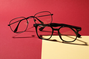 Two pairs of stylish eyeglasses on color background