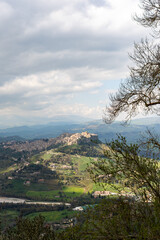 Naklejka premium Scenic view of Enna, Sicily showcasing a historic hilltop castle surrounded by lush green fields and distant mountains under a cloudy sky