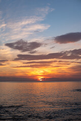 Obraz premium Vibrant sunset over calm ocean waters with colorful clouds reflecting on the surface, creating a serene coastal landscape at dusk