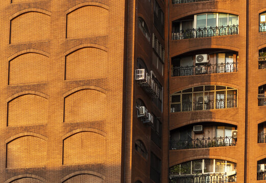 View of the red brick facade of a residential building with arched balconies and air conditioning units under warm sunlight Taipei City, Taiwan.