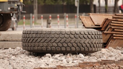 Zużyta opona maszyny budowlanej leżąca na podłożu z kruszywa na terenie budowy, otoczona materiałami takimi jak drewniane deski i elementy stalowe, ukazująca surowy charakter prac inżynieryjnych © tomo81