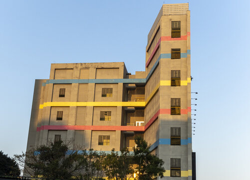 View of a modern concrete building featuring vibrant horizontal stripes of blue, yellow, and pink under a clear sky with green trees in the foreground Taipei City, Taiwan.