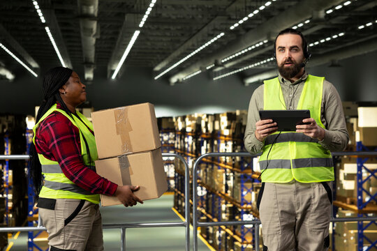 Customer service agent using headset for phone calls related to cargo status and express delivery, working in a warehouse fulfillment center. Worker verifying tracking numbers on tablet.