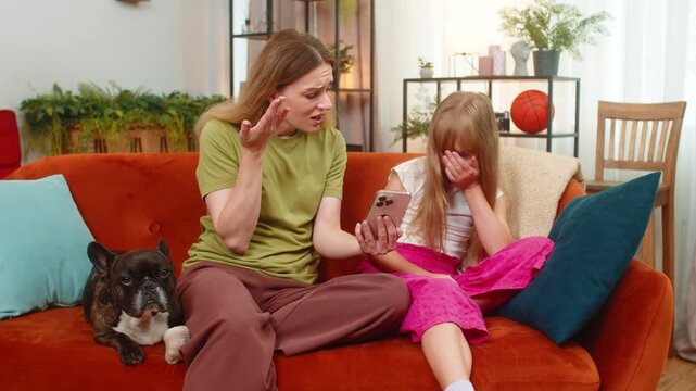 Mother and daughter lose game with French bulldog at home using smartphone shrug frown feeling upset. Woman, girl with dog on sofa react to fail game retry tap screen seek help support very sad mood