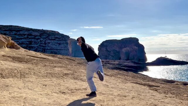 Energetic man jumpstyle dancing on sunny ocean cliffs