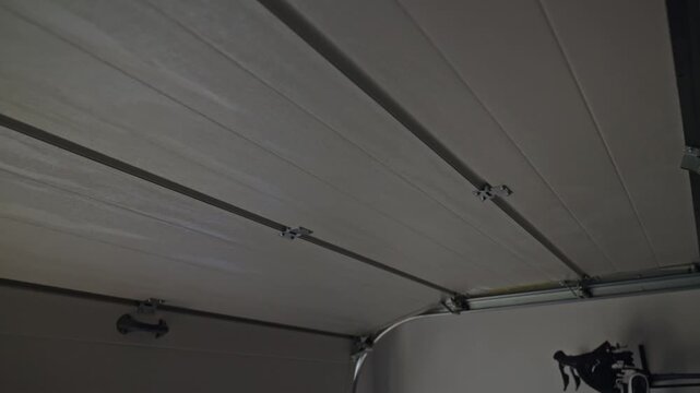 Sectional garage door is opening from inside with track, hinge and pull cord visible. Concept of door mechanism and home security