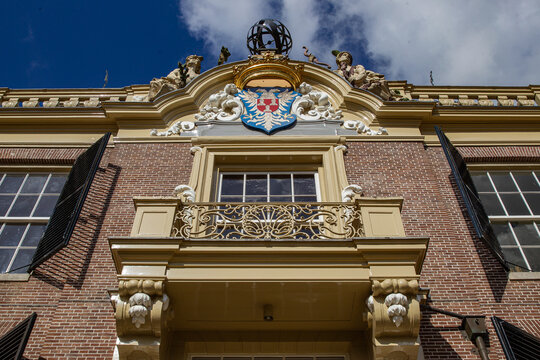 View of Castle Groeneveld facade featuring an ornate balcony and heraldic coat of arms against a blue sky in Baarn, Utrecht, Netherlands.