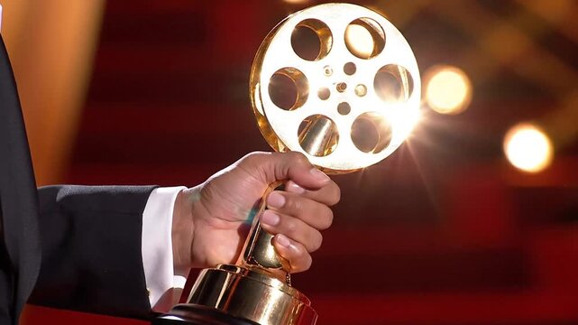 Hand holding golden film reel trophy at awards ceremony