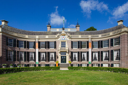 View of the historic curved facade of Castle Groeneveld with its black shutters and white window frames under a blue sky in Baarn, Utrecht, Netherlands.