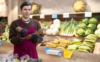 Fototapeta premium Adult man seller in apron with cassava in vegetable shop
