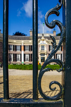 View of Castle Groeneveld seen through the ornate scrollwork of a black wrought iron gate under a clear blue sky Baarn, Utrecht, Netherlands.