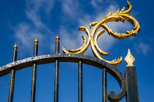 View of the ornate gilded scrollwork on the black wrought iron gate of Castle Groeneveld under a bright blue sky in Baarn, Utrecht, Netherlands.