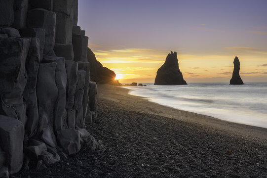 View of Reynisfjara Beach featuring basalt columns and Reynisdrangar sea stacks at sunset over the black sand shore in Reynisfjara, Myrdalshreppur, Iceland.