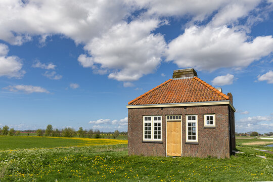 View of the historic brick building of Schokland surrounded by green meadows with yellow wildflowers under a bright blue sky with white clouds Schokland, Flevoland, Netherlands.