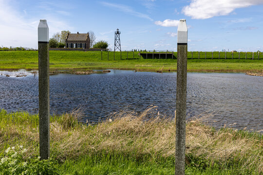 View of the historic Middelbuurt house and lighthouse frame across a marshy landscape with wooden poles in Schokland, Flevoland, Netherlands.
