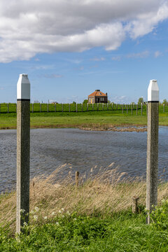 View of the historic former island of Schokland with wooden poles, a calm pond, and a traditional brick house on a grassy embankment Schokland, Flevoland, Netherlands.