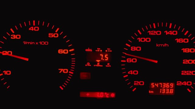 Luminous red car dashboard at night with the speedometer needle moving, indicating acceleration, and the tachometer showing engine revs while driving on a cold winter day