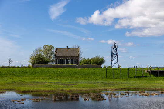View of the historic lighthouse keeper's house and iron lighthouse tower on the former island of Schokland with green meadows and marshy water under a blue sky Schokland, Flevoland, Netherlands.