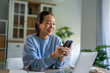Asian woman multitasking using smart phone and laptop for remote work