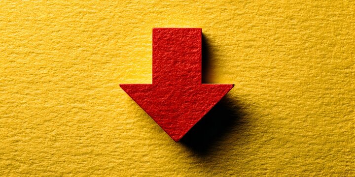 Red arrow points down on textured yellow surface suggesting decrease or decline, a simple direction indicator for charts or graphs.