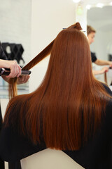 Fototapeta premium Stylist straightening girl's hair in beauty salon, closeup