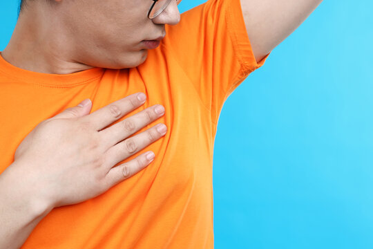 Young guy with sweaty armpits on light blue background, closeup. Space for text