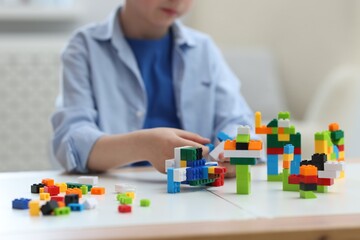 Fototapeta premium Construction toy. Little boy playing with building blocks at table indoors, closeup