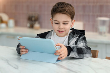 Naklejka premium Little boy using modern tablet at white marble table indoors