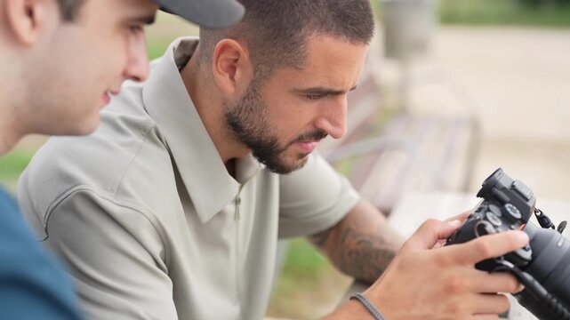 Two men examine camera settings together. One man holds the device attentively. Their focus suggests shared learning or planning. Ideal for photography tutorials or team collaboration scenes