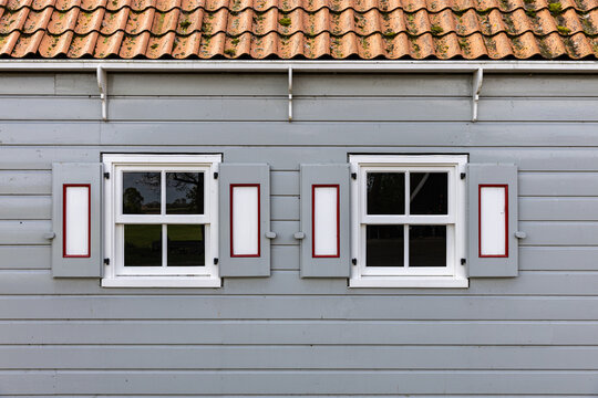 View of the traditional wooden facade of a historic building featuring grey siding and white-framed windows with decorative shutters in Schokland, Flevoland, Netherlands.