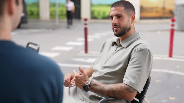 Man sits in chair, engaged in conversation. He gestures actively, showing interest and thoughtfulness. His calm demeanor suggests relaxed, meaningful dialogue. Perfect for interviews
