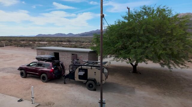 Aerial view shows SUV with a teardrop camper at a campsite in Baja California along a river.