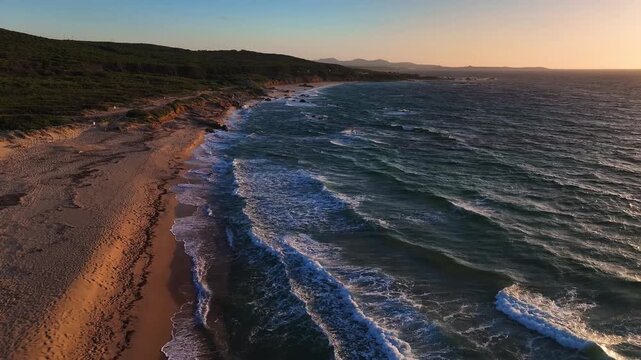 Aerial view of the sandy beach and waves crashing on the shore at sunset in Costa Paradiso, Sardegna, Italy.