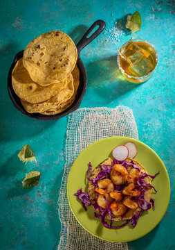 Overhead photo of shrimp taco with drink, corn tortillas