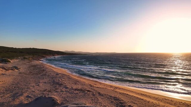 Aerial view of the golden sand dunes and turquoise sea waves during sunset at Costa Paradiso, Sardegna, Italy.