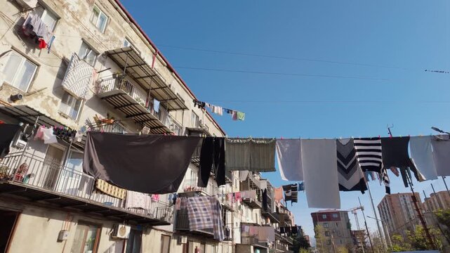Colorful laundry hanging on clotheslines between old residential buildings in a poor urban area. The clothes are waving in the wind against a clear blue sky, illustrating daily life in a ghetto