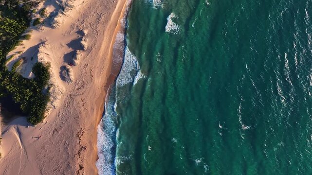 Aerial view of the turquoise Mediterranean sea waves crashing on the sandy beach of Costa Paradiso with green vegetation and dunes, Costa Paradiso, Sardegna, Italy.