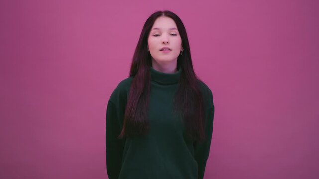 Portrait: teenage girl on pink background in green sweatshirt. Brunette woman face takes deep breath. Beautiful female, generation Z, alpha. Calm emotion and mindfulness, peaceful moment of relaxation