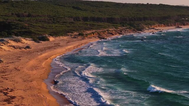 Aerial view of the rugged coastline with a sandy beach and turquoise waves at Costa Paradiso, Sardegna, Italy.