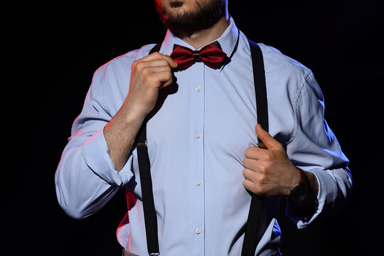 Handsome man with suspenders and bow tie on dark background