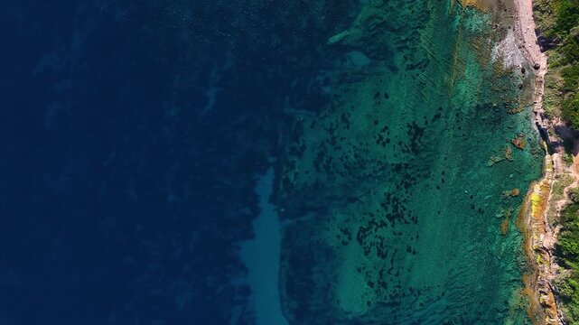 Aerial view of the crystal clear turquoise waters and rugged rocky coastline with submerged reefs in Costa Paradiso, Sardegna, Italy.