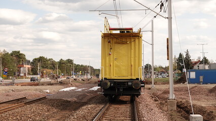 Żółty wagon techniczny stoi na torowisku podczas prac modernizacyjnych linii kolejowej. Nad szynami widoczna jest sieć trakcyjna, a w oddali trwają intensywne roboty przy infrastrukturze kolejowej © tomo81