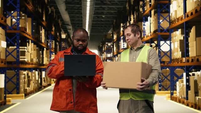 Coworkers arranging cardboard boxes on shelves and doing inventory on laptop, distribution center efficiency depends on workforce collaboration and safety. Logistics management systems.
