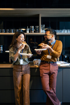 Cheerful colleagues enjoying pizza and social interaction during office break, fostering workplace bonding in modern kitchen